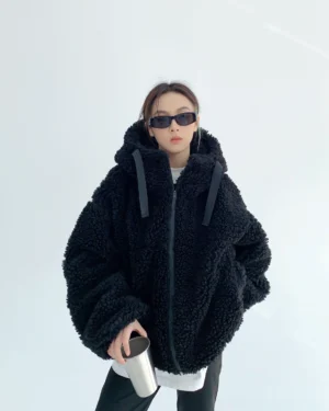 Front view of a woman wearing a black oversized sherpa teddy zip hoodie with fluffy curly fleece, dropped shoulders, hood drawstrings, and full front zipper