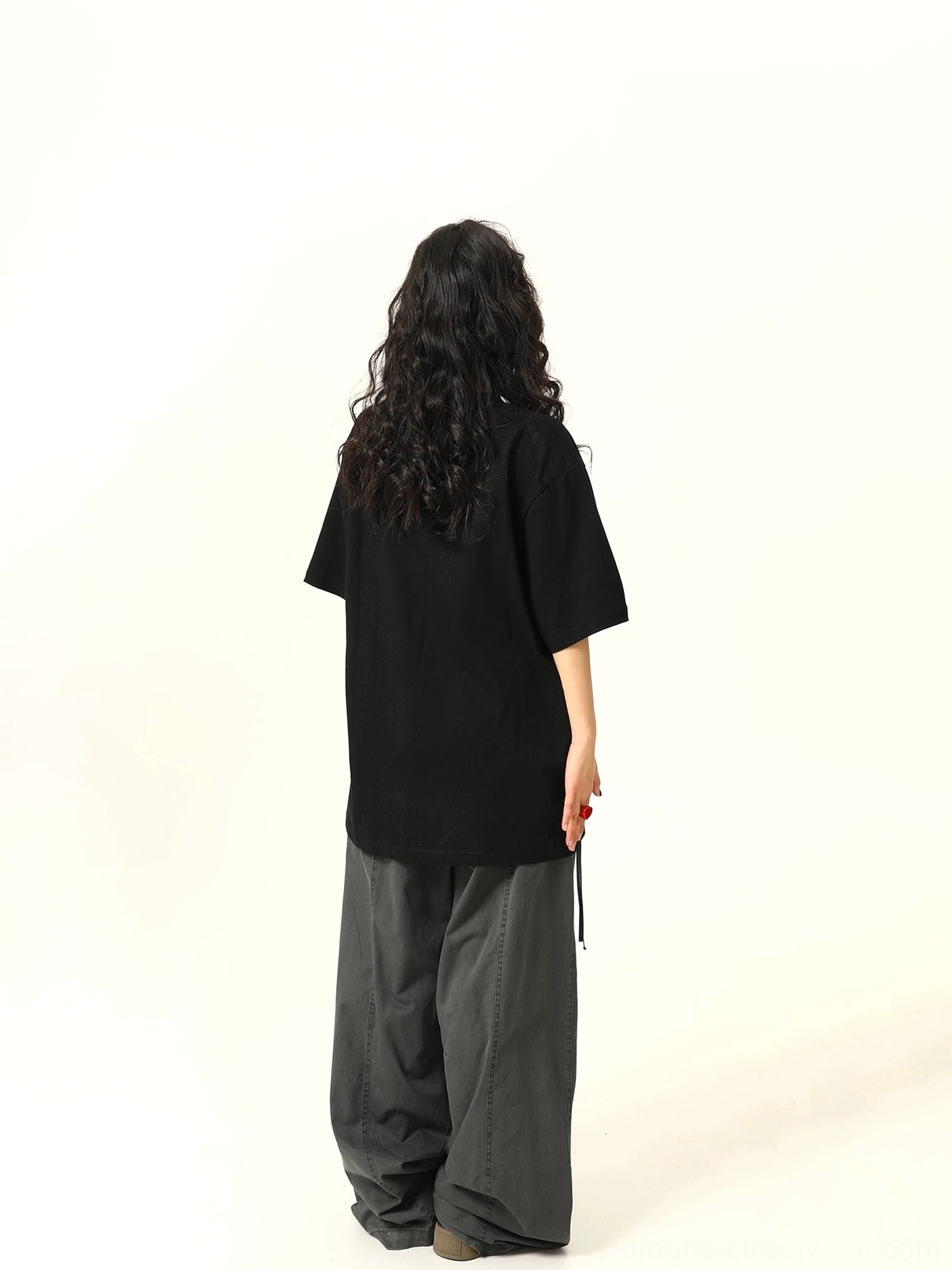Back view of a black oversized solid crew neck T-shirt showing the relaxed loose silhouette and short sleeves with dark cargo pants