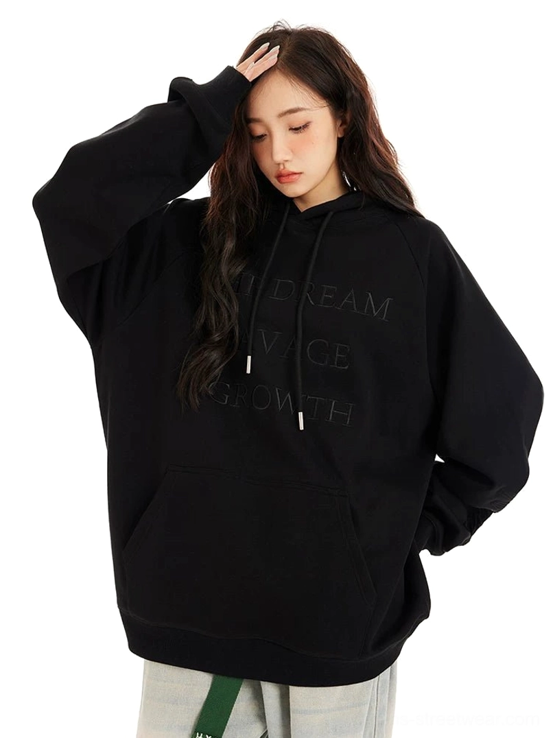 Black oversized streetwear hoodie with raised embossed chest lettering, kangaroo pocket, roomy hood, and relaxed fit styled with denim