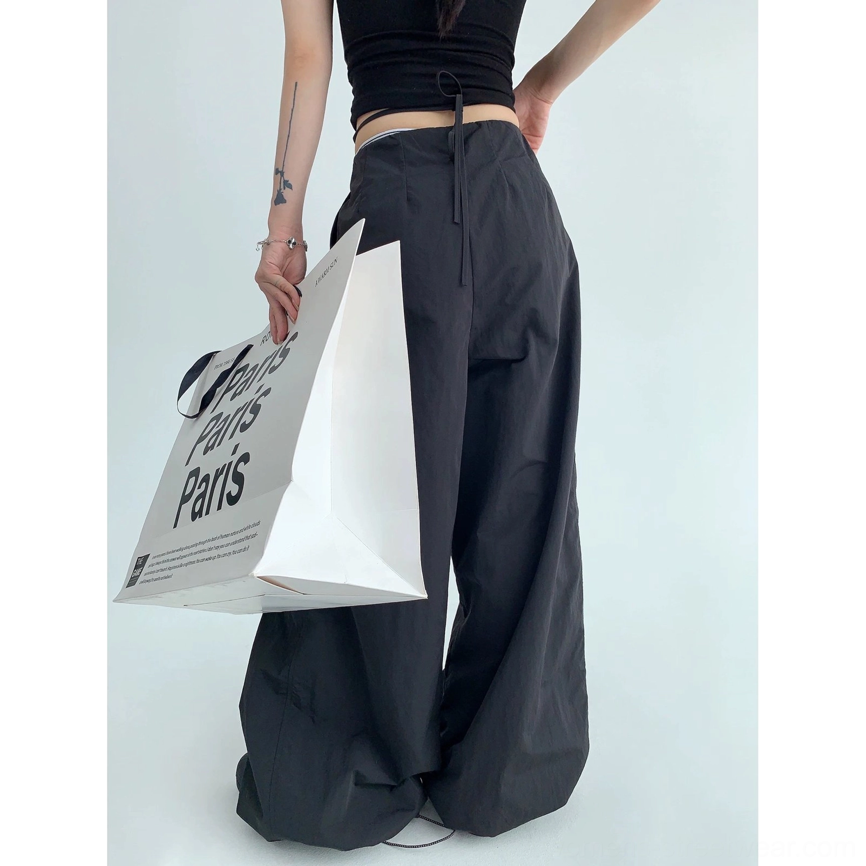 Black oversized streetwear parachute pants shown from the side back view with relaxed wide legs and subtle tapered hem