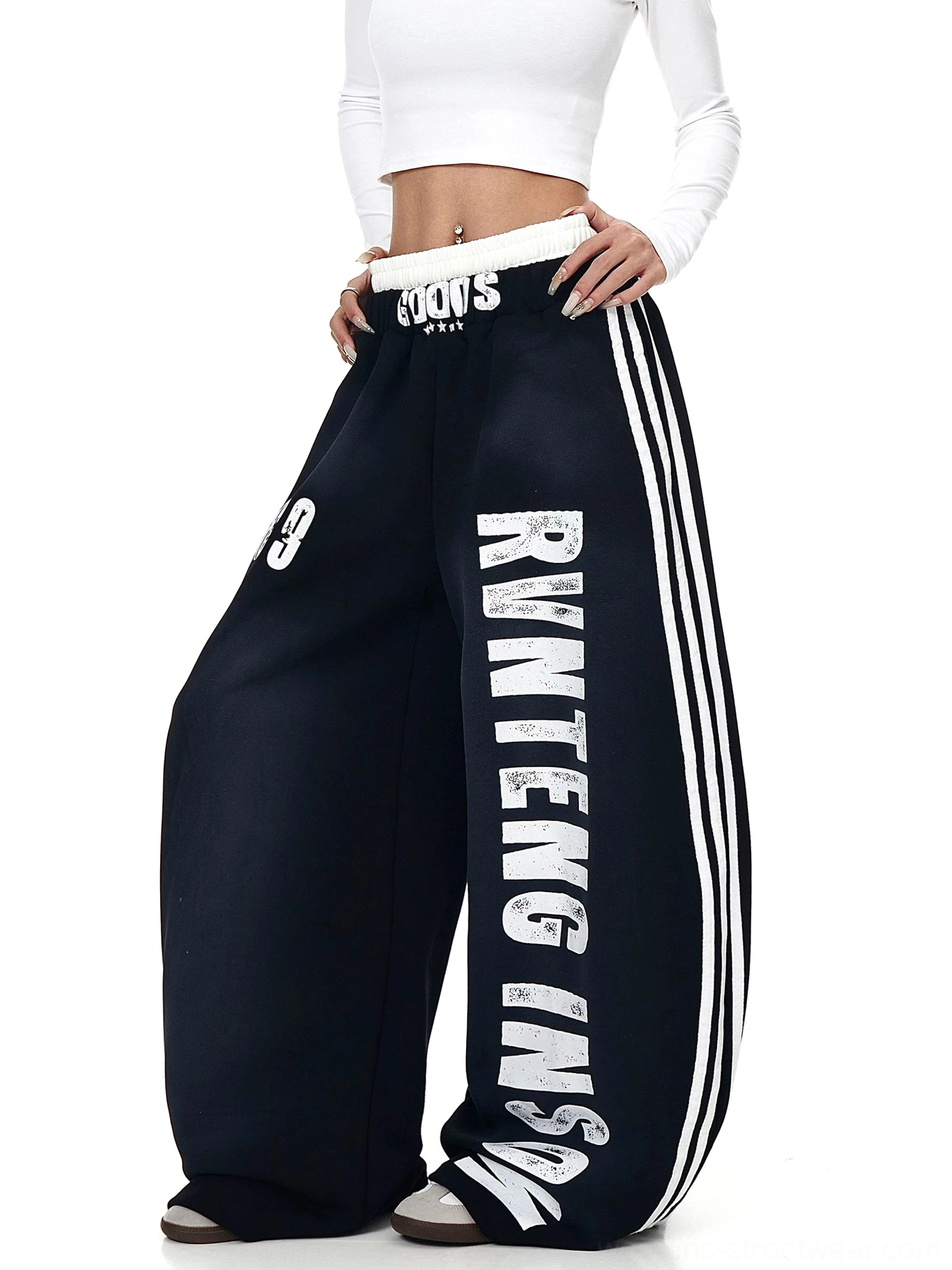 Three-quarter view of black oversized streetwear sweatpants with vertical lettering, single 9 graphic, wide legs, and contrast side stripes