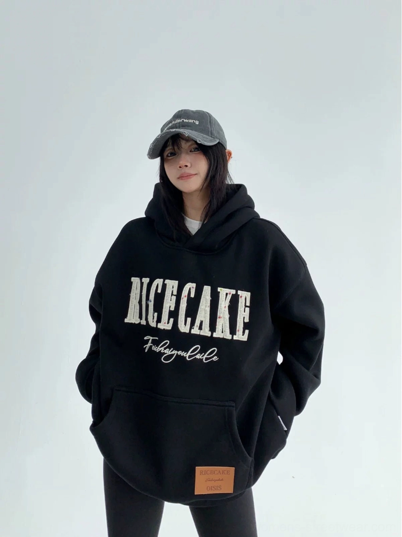 Black oversized varsity graphic hoodie styled with a baseball cap, fitted pants, and sneakers for a modern streetwear outfit