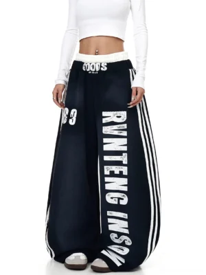 Black oversized wide-leg fleece sweatpants styled with a white cropped top, reversed vertical lettering, 89 graphic, and athletic side stripes