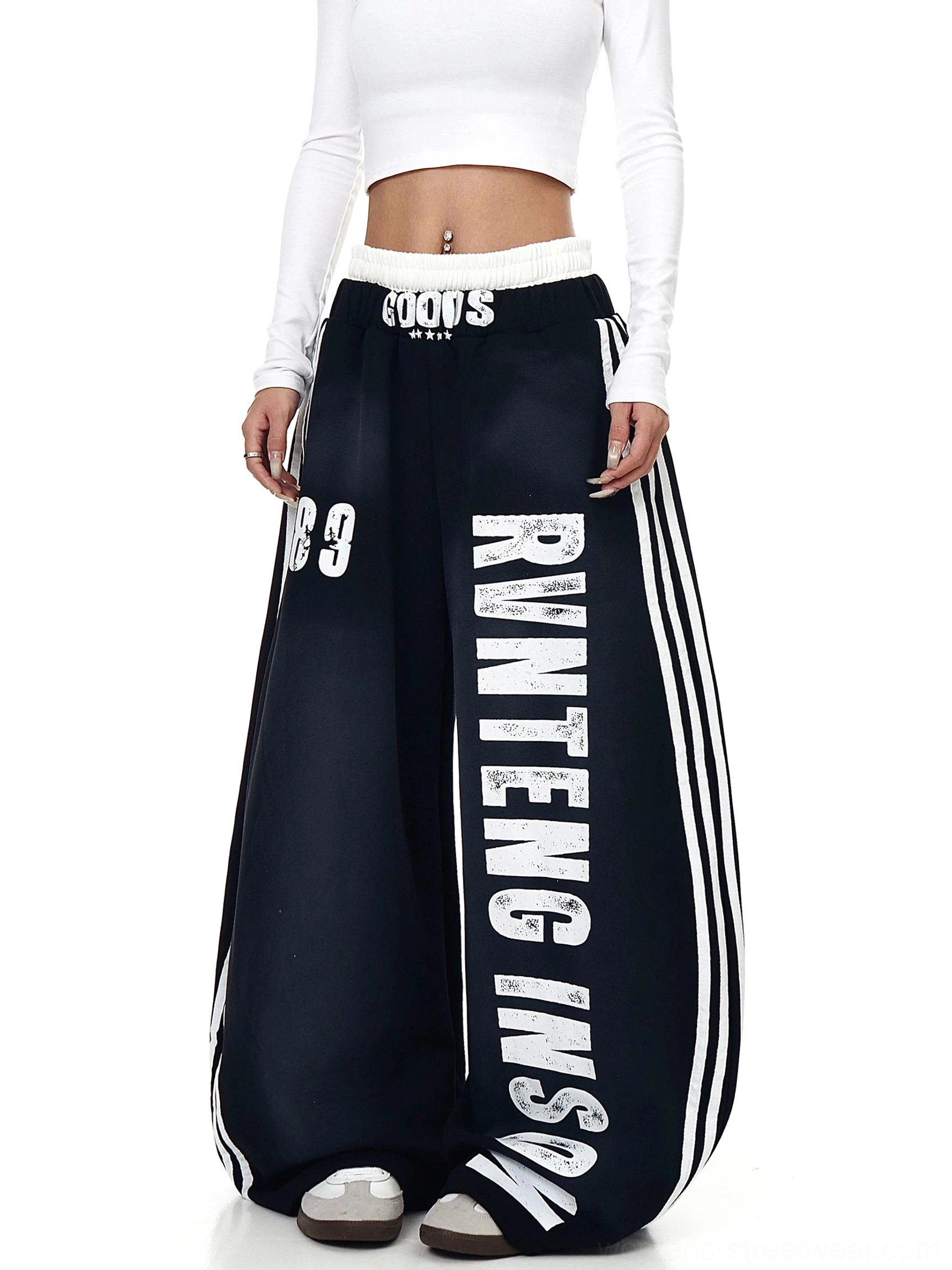 Black oversized wide-leg fleece sweatpants styled with a white cropped top, reversed vertical lettering, 89 graphic, and athletic side stripes