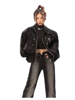 Black oversized faux leather bomber jacket on a female model with glossy finish, snap buttons, embroidered chest detail, black crop top, and wide leg jeans