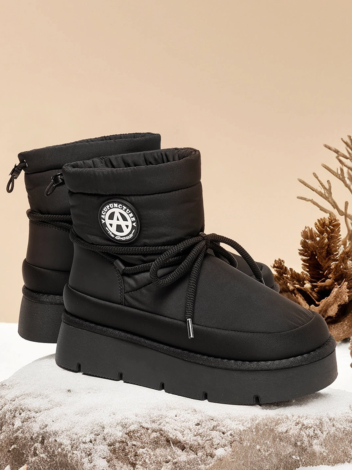 Black padded platform snow boots on faux snow showing the closed padded collar, heel pull tab, and chunky sole