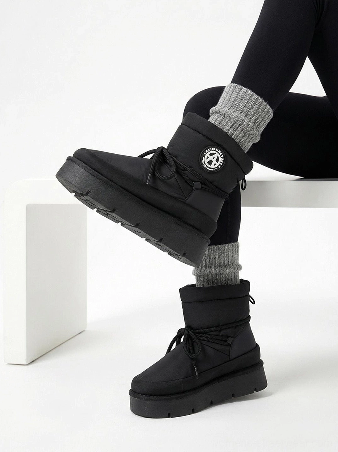 Black padded platform snow boots worn with black leggings, showing angled side view and oversized wrap lace details