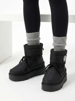 Model wearing black padded platform snow boots with gray crew socks and black leggings in a front view