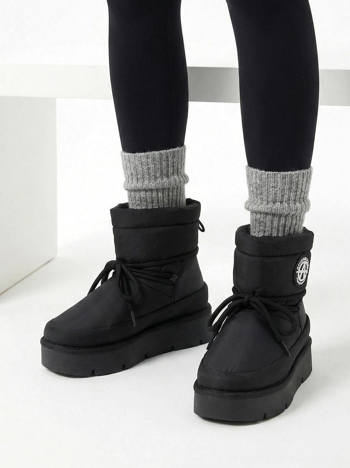 Model wearing black padded platform snow boots with gray crew socks and black leggings in a front view