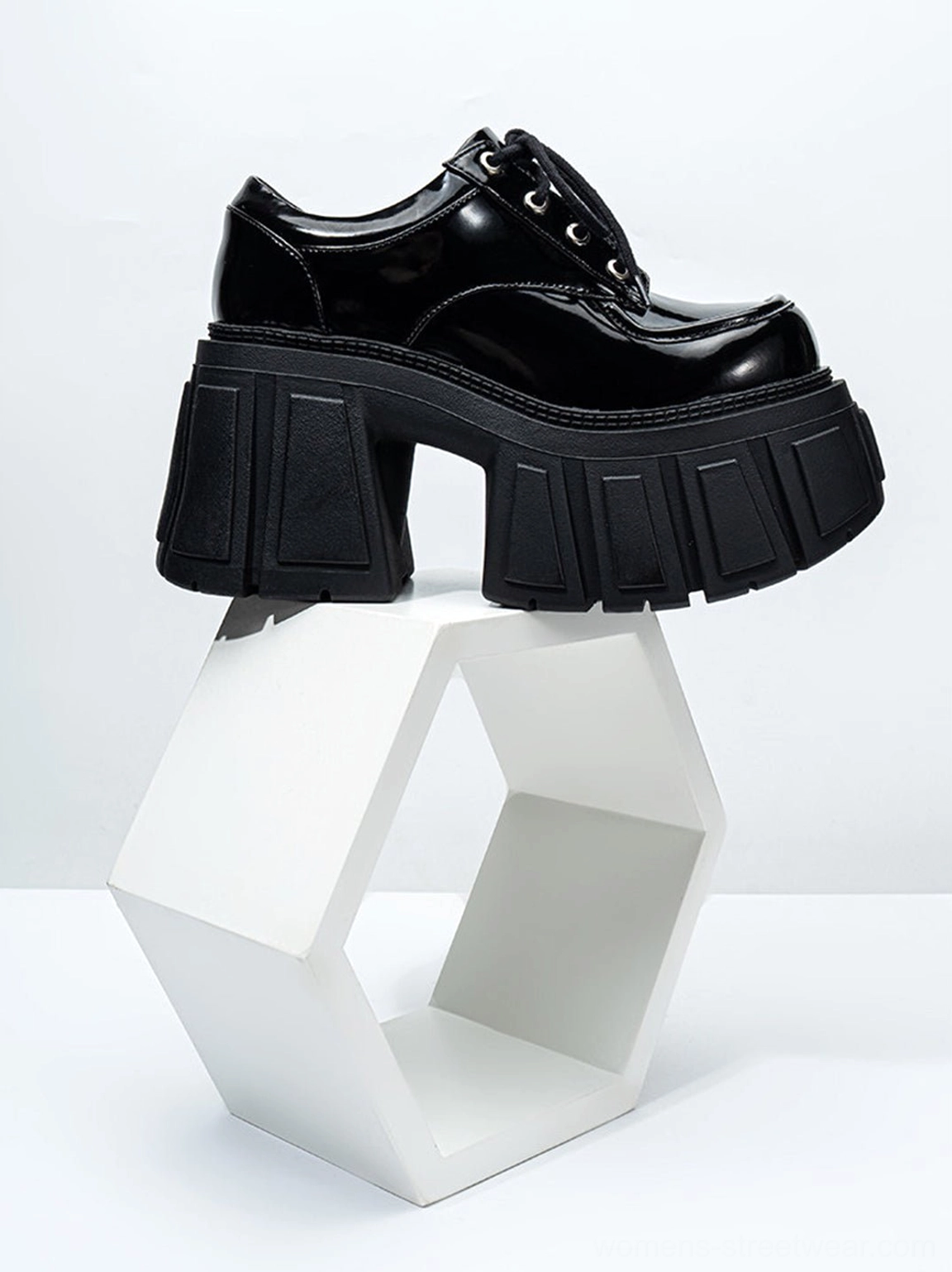 Black patent chunky platform derby heel displayed on a white hexagonal prop with architectural block heel