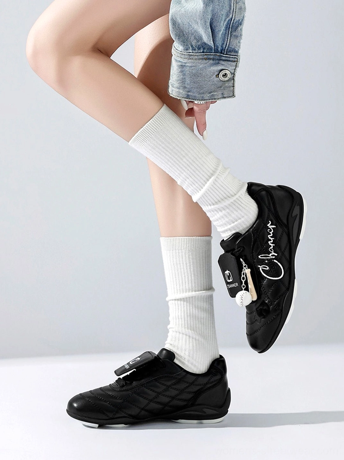 Side profile of black quilted patent foldover tongue retro sneaker styled with white socks and denim