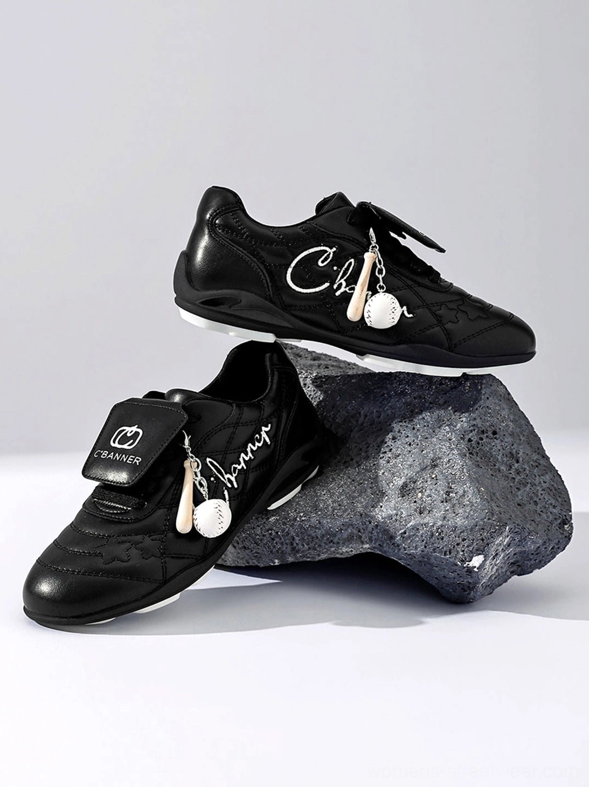 Pair of black patent foldover tongue retro streetwear sneakers displayed on grey studio rock prop