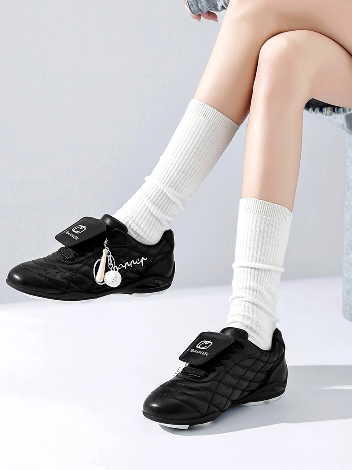 Top view of black foldover tongue retro sneakers worn with white socks showing decorative metallic charm