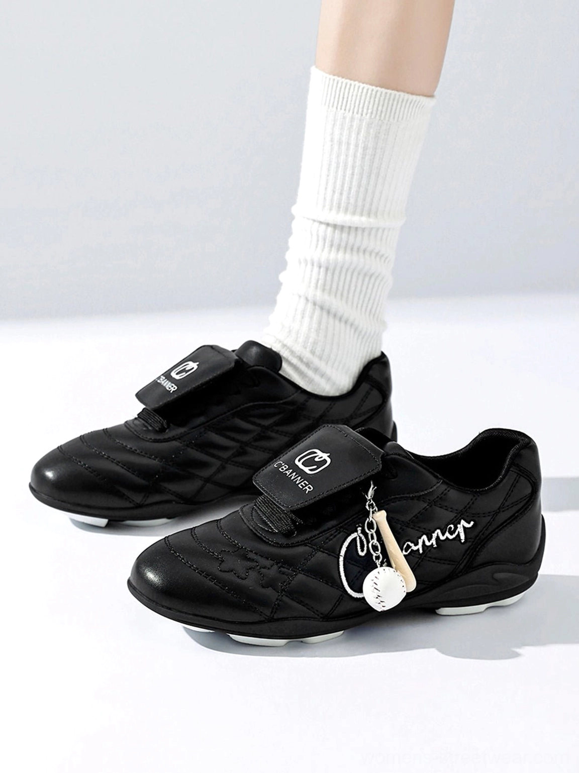 Pair of black patent foldover tongue retro streetwear sneakers with metallic charm on white background