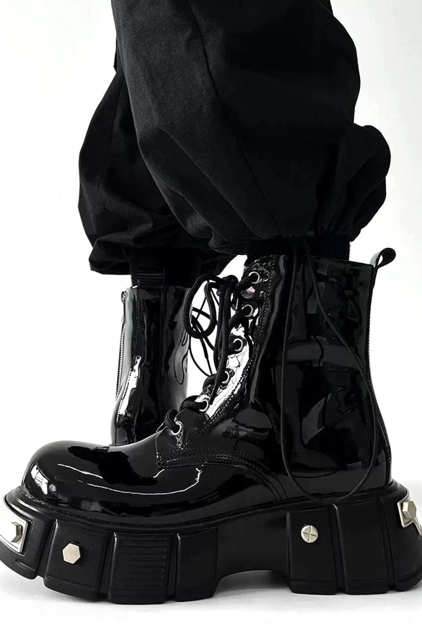 Side three-quarter view of a black patent leather platform combat boot worn with cropped black cargo pants, showing the glossy upper, laces, rear pull tab, and chunky sole