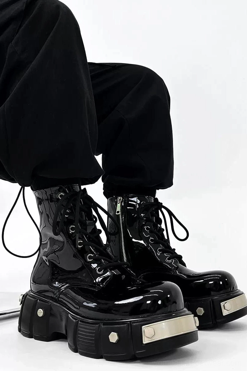 Front three-quarter view of black patent leather platform combat boots worn with black cargo pants, showing glossy lace-up uppers, silver hardware, and heavy lug platform soles