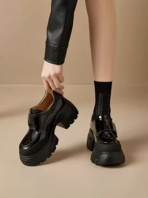 Female model wearing glossy black platform Mary Jane shoes with fishnet socks and leather streetwear outfit