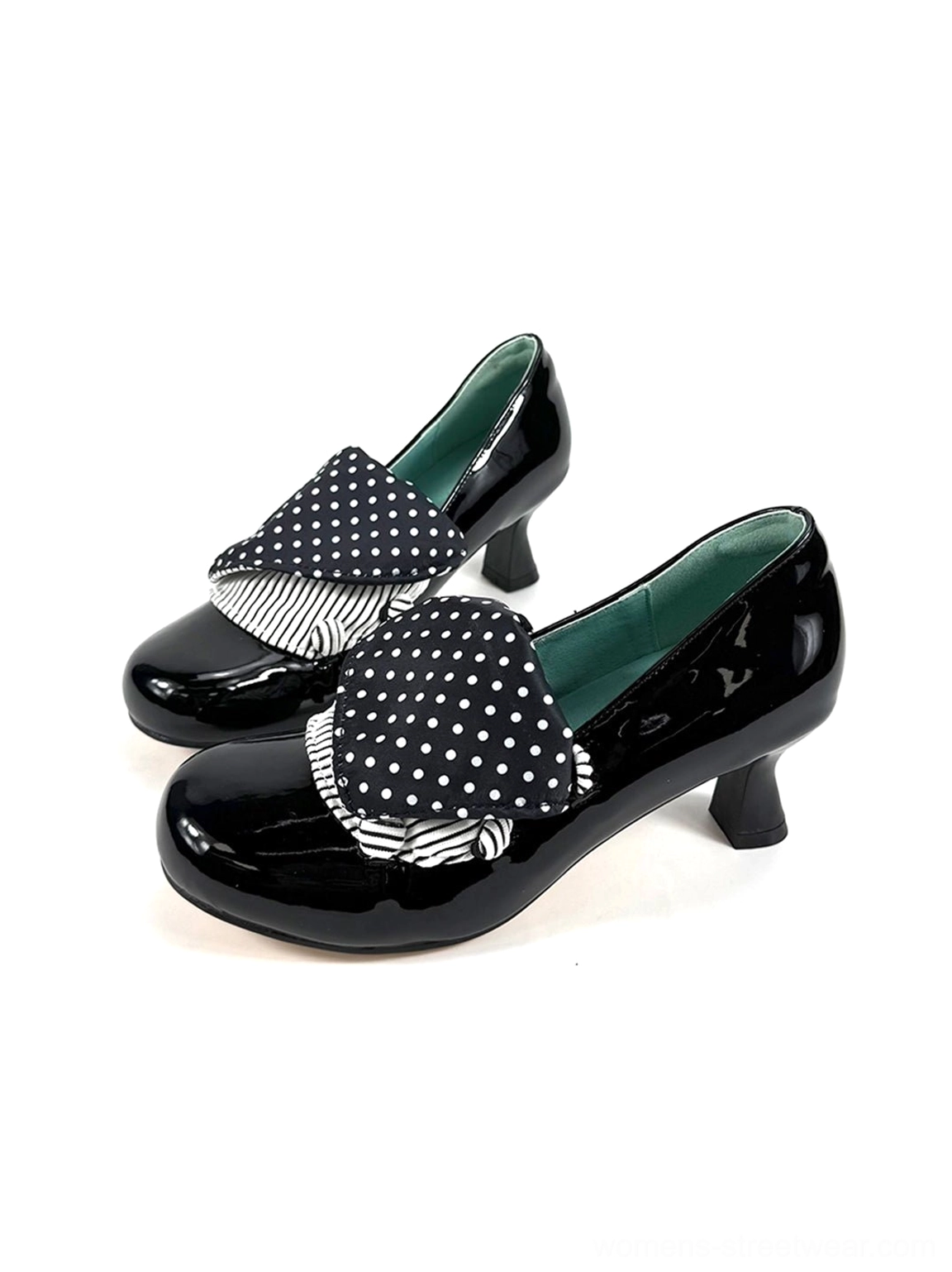 Three-quarter front view of black patent mid-heel pumps featuring oversized polka dot bows and rounded toes