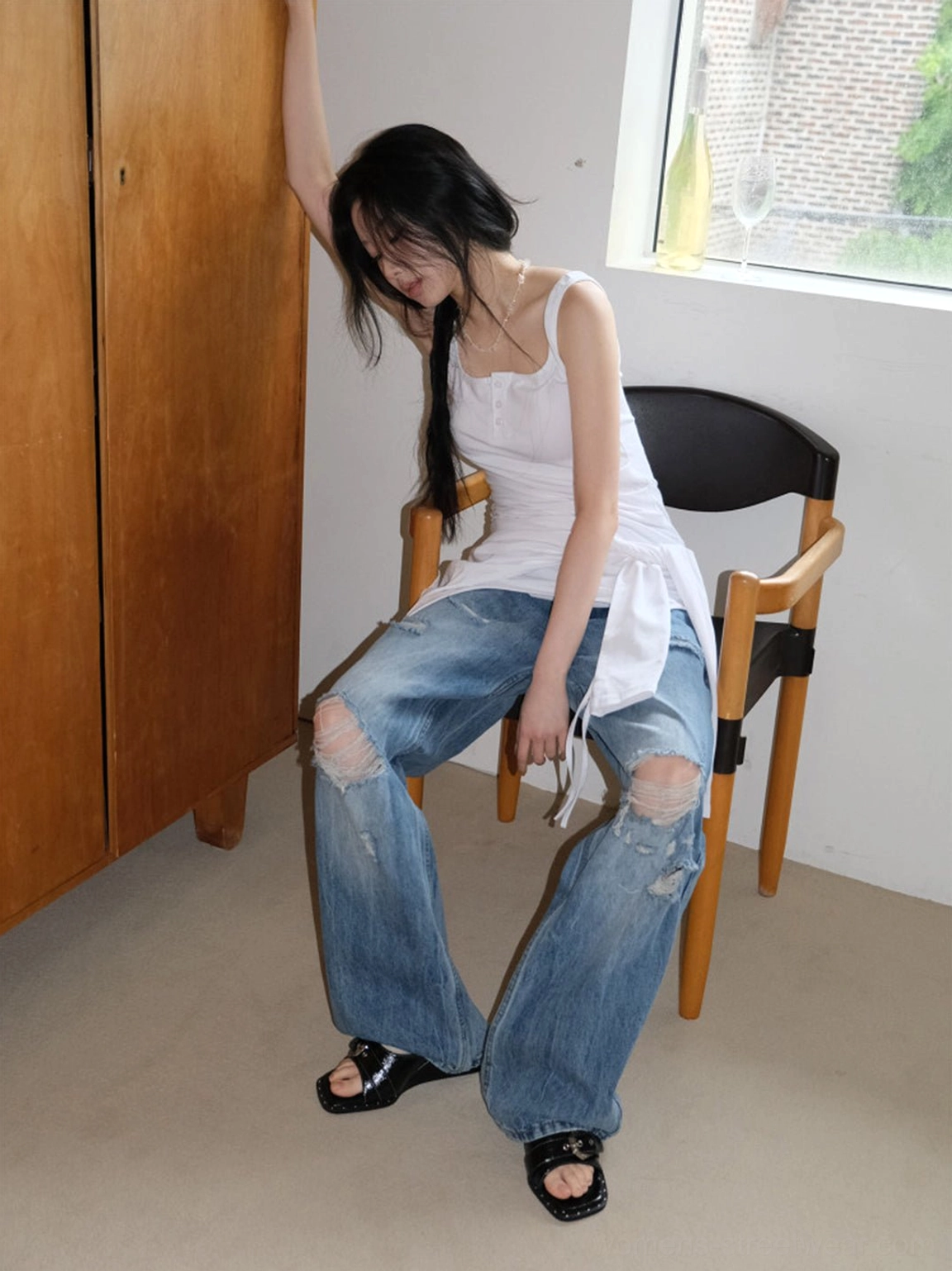 Seated model styling black patent square-toe wedge slide sandals with ripped denim and a white tank top