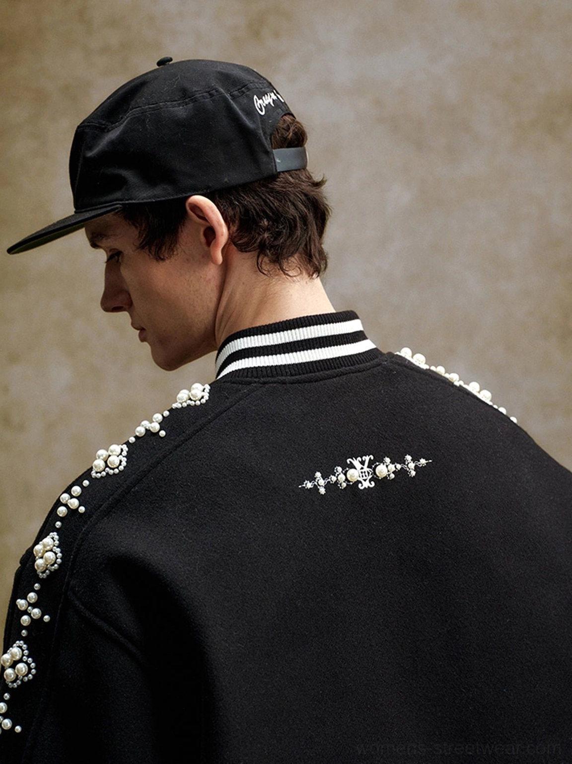 Detailed back shoulder view of black pearl beaded varsity jacket showing embroidered motif pearl trim and striped ribbed collar