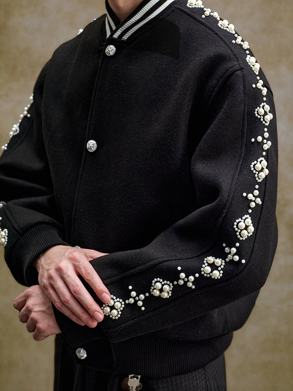 Close-up of black varsity jacket shoulder and sleeve with pearl crystal-style beading silver snap buttons and ribbed collar