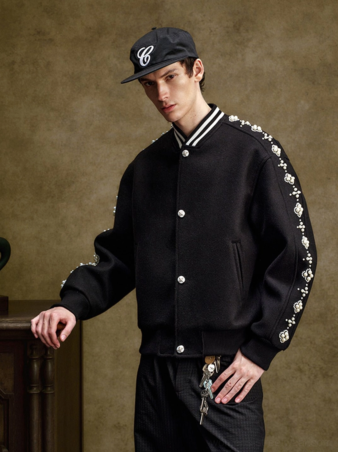Model wearing a black pearl beaded varsity jacket with baseball cap and black trousers in a Korean streetwear outfit