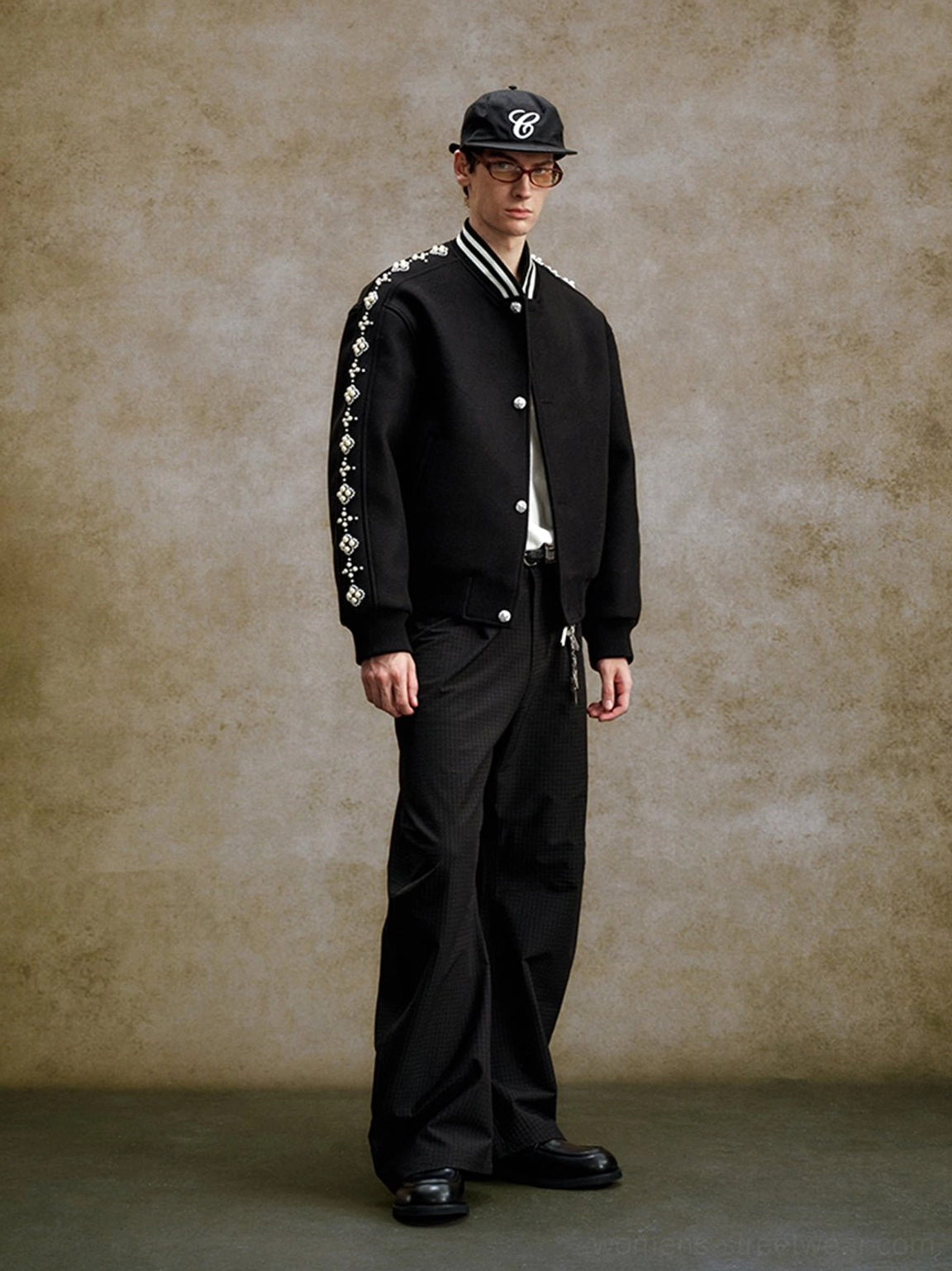 Full body styling of a relaxed black pearl beaded varsity jacket with cap and tailored black trousers