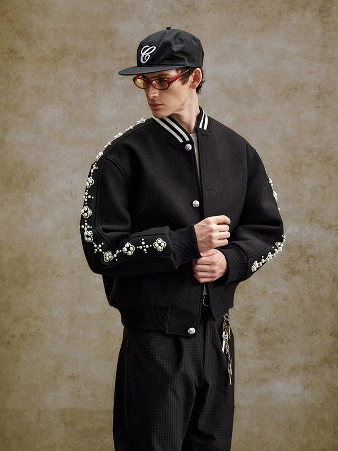 Side view of black pearl beaded varsity jacket with striped ribbed cuffs silver snap buttons and embellished sleeves