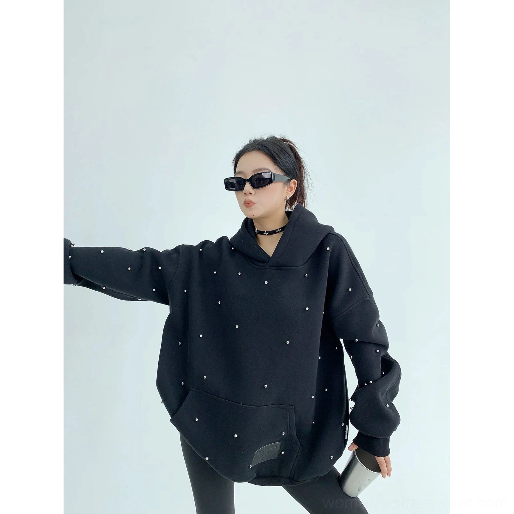 Black pearl-decorated oversized hoodie shown in a dynamic side view with loose extended sleeves and scattered pearl-style studs