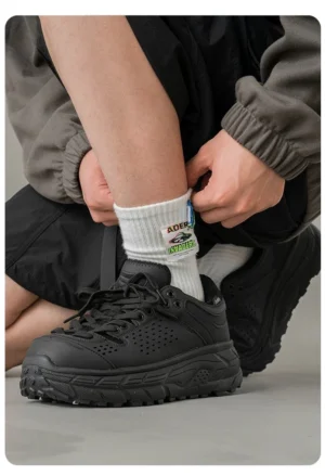 Black perforated utility outdoor trainers being put on with a street workwear outfit, featuring lace-up closure and rugged chunky traction outsole