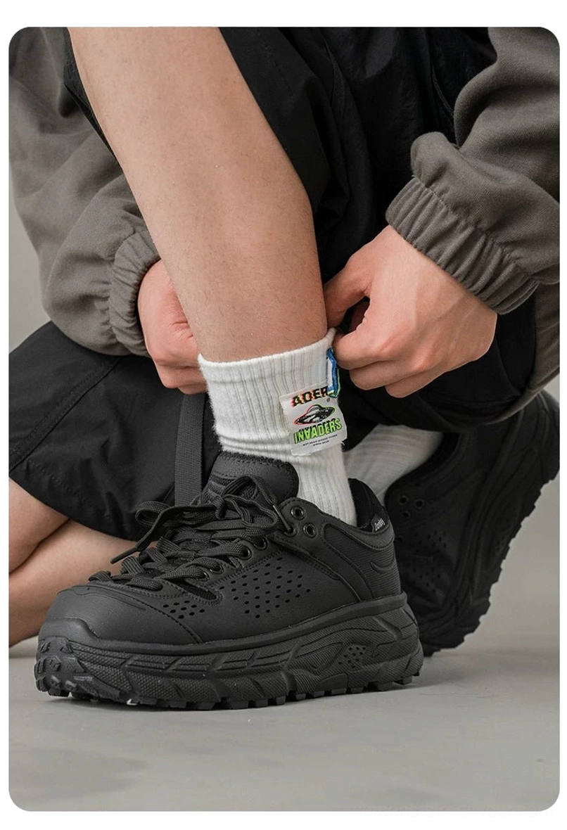 Black perforated utility outdoor trainers being put on with a street workwear outfit, featuring lace-up closure and rugged chunky traction outsole