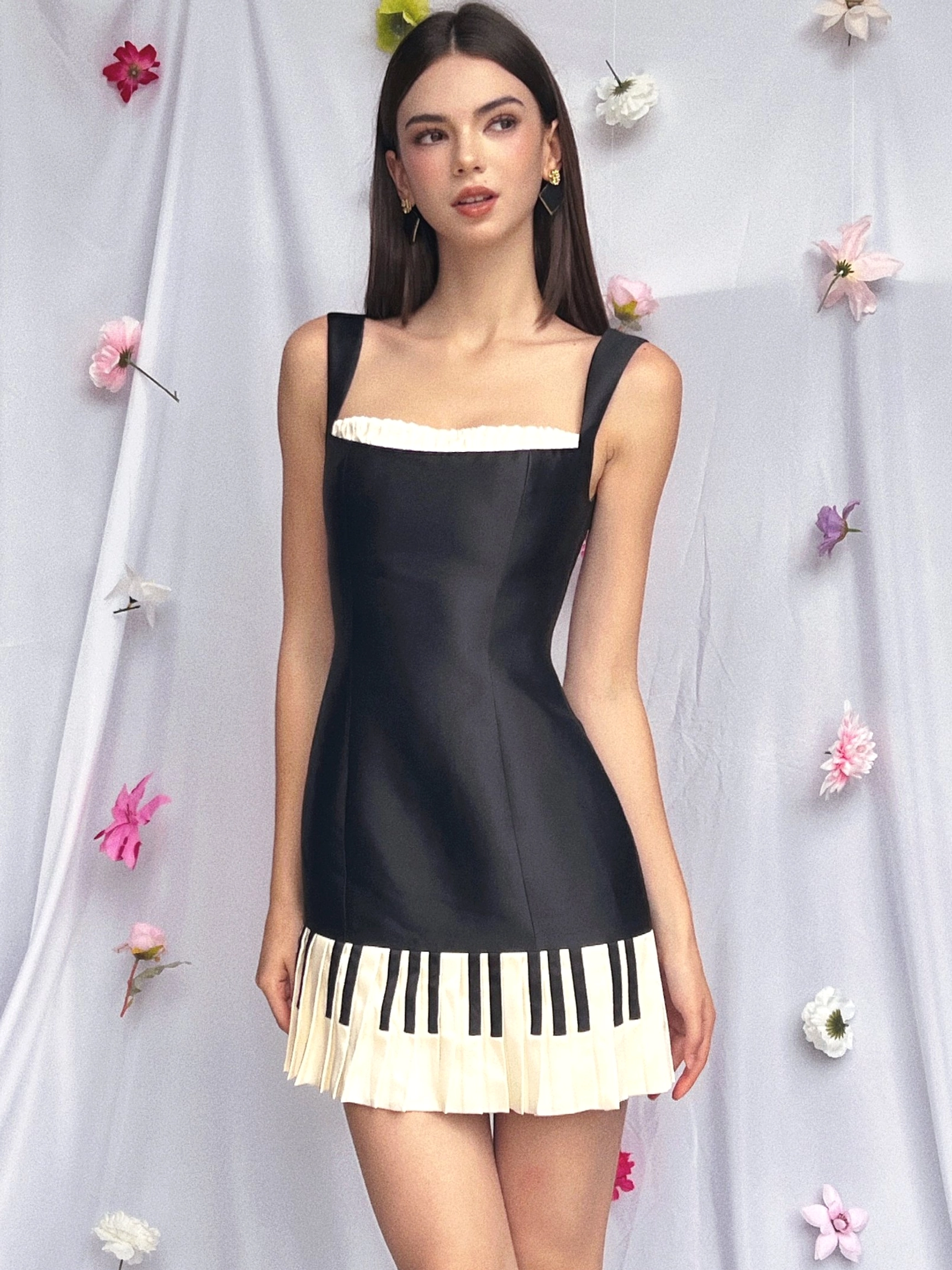 Front view of black piano keys mini dress with slim shoulder straps fitted bodice and off-white pleated hem with black piano key print