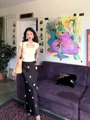 Three-quarter view of a black floral print maxi skirt with delicate pink flowers and flowing satin-like viscose texture