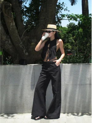 Black pinstripe high-waisted wide-leg streetwear trousers styled with a cropped black halter top in a full-body front view