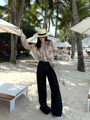 Black pinstripe wide-leg trousers styled with a sheer printed long-sleeve shirt in a polished resort streetwear outfit