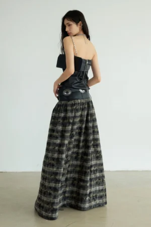 Back view of a floor length black plaid maxi skirt styled with a strapless leather corset outfit and gathered tartan fabric