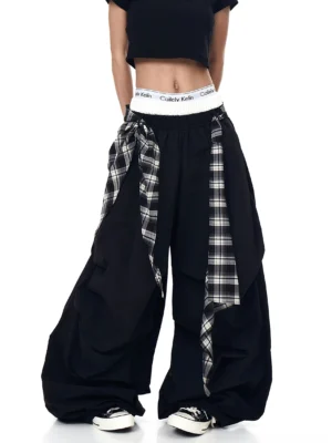 Rear three-quarter view of black plaid parachute pants with long side drape panels, wide ballooned legs, and relaxed Korean streetwear styling