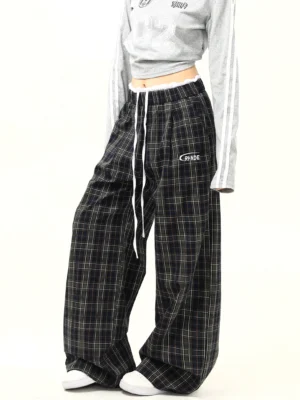 Side view of black plaid wide-leg streetwear pants showing the oversized silhouette, front pleats, adjustable drawstring waistband, embroidered detail, and casual Korean fashion styling