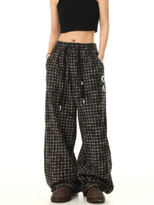 Front view of black plaid wide-leg streetwear track pants with elastic drawstring waist side pockets and graphic badge details styled with a black crop top