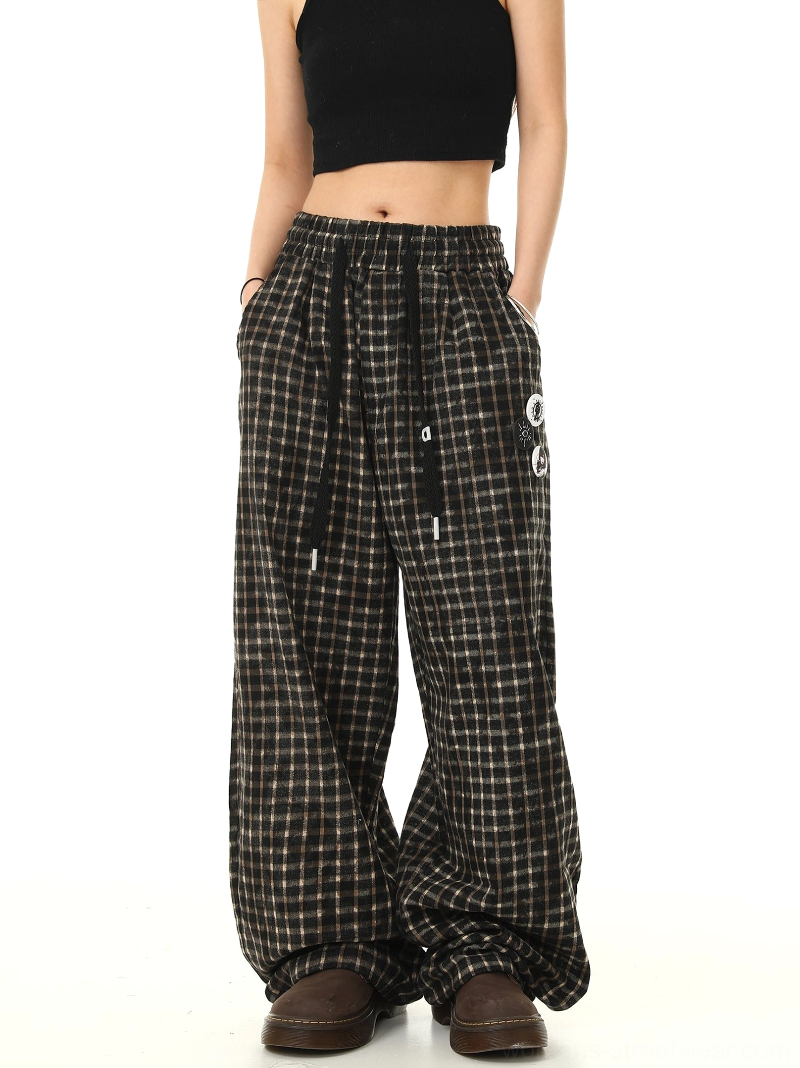 Front view of black plaid wide-leg streetwear track pants with elastic drawstring waist side pockets and graphic badge details styled with a black crop top