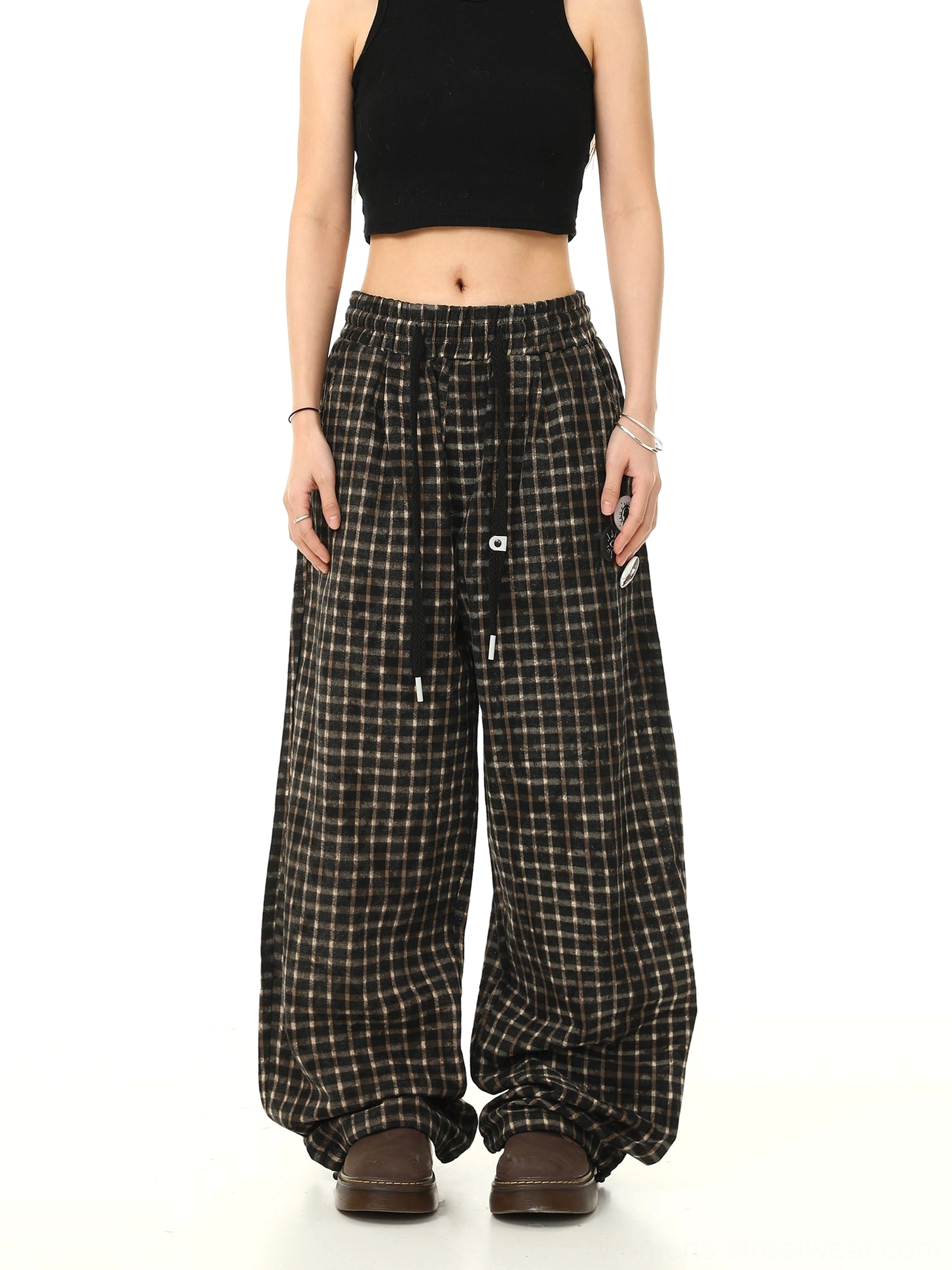 Front full-body view of black plaid wide-leg track pants with drawstring waistband graphic patches and oversized streetwear proportions