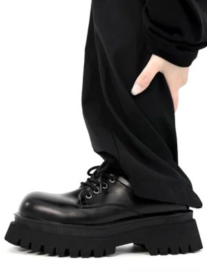 Side profile of black platform derby shoes styled with wide-leg trousers, featuring a polished upper, chunky ridged outsole, and low-top lace-up derby shape