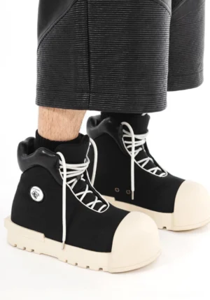 Model wearing black sculpted-toe platform high-top boots with white contrast laces, oversized off-white toe caps, cropped leather pants, and black crew socks