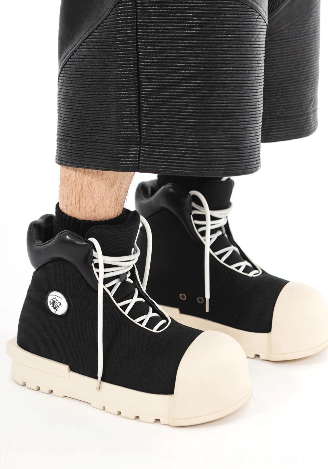 Model wearing black sculpted-toe platform high-top boots with white contrast laces, oversized off-white toe caps, cropped leather pants, and black crew socks