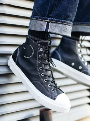 Black platform high-top streetwear sneakers worn with cuffed dark denim, featuring white contrast stitching, printed upper details, and a thick white rubber midsole