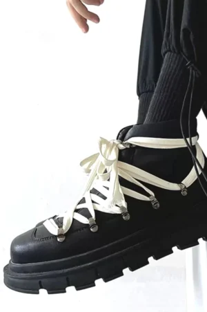 Black platform hiking combat boot worn with cropped black trousers and thick socks, featuring dual lace straps, metal hardware, and high-top streetwear styling