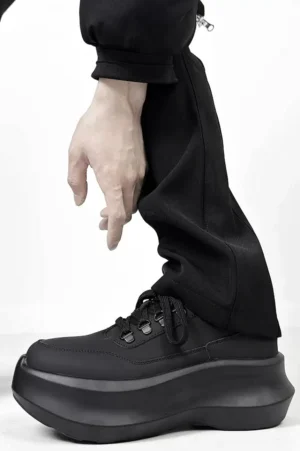 Black platform lace-up sneakers worn with long black trousers showing the raised thick sole and sleek matte leather upper