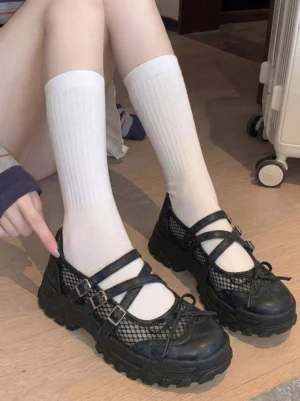 Black platform Mary Jane sneakers worn with white crew socks on a wooden floor, showing the chunky streetwear silhouette and everyday fit