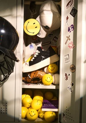 Black and white platform skate sneaker displayed inside a sticker-covered locker with baseball gear and playful streetwear accessories