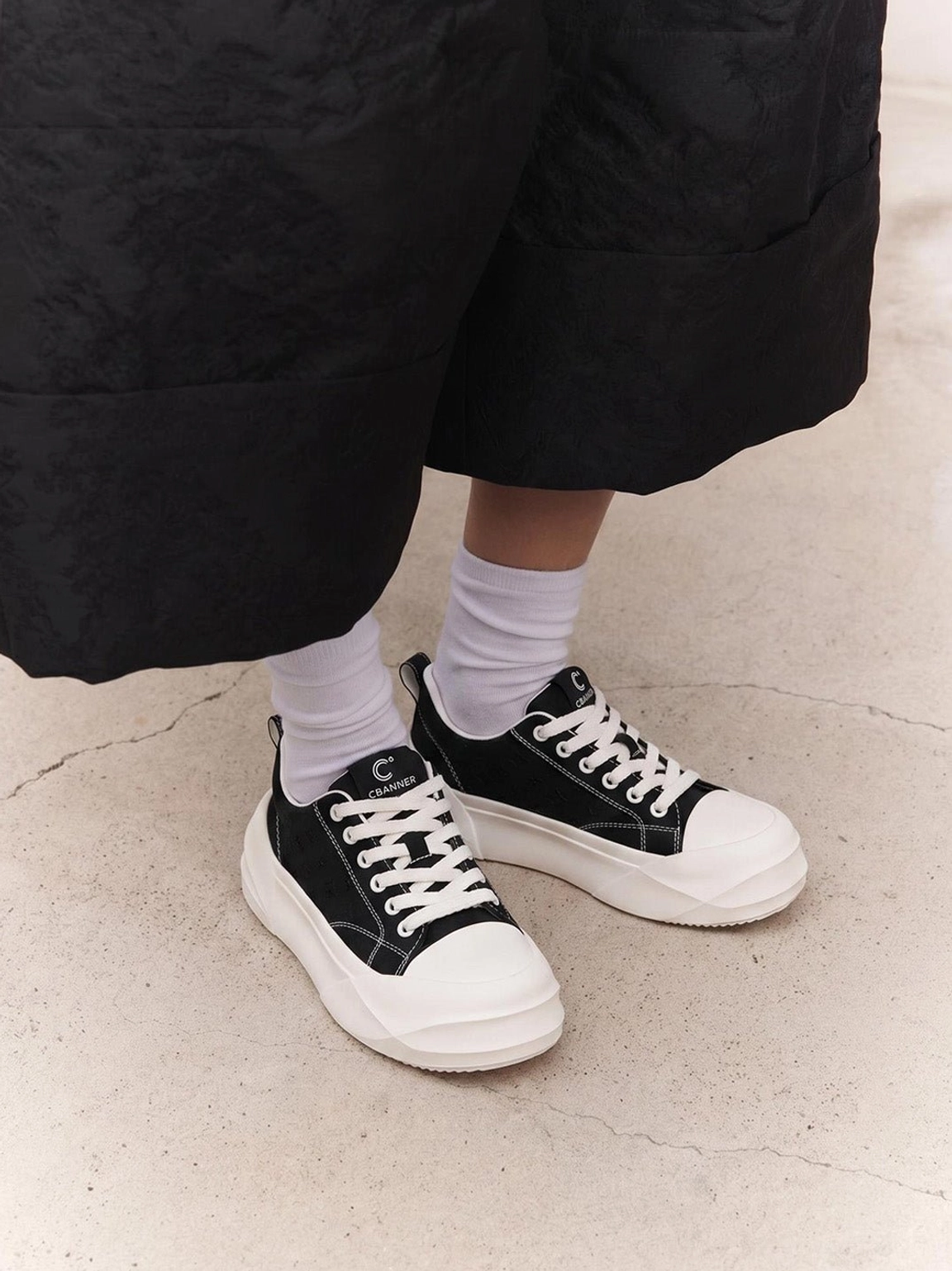 Black platform skate sneakers with white geometric sole worn with wide leg black pants